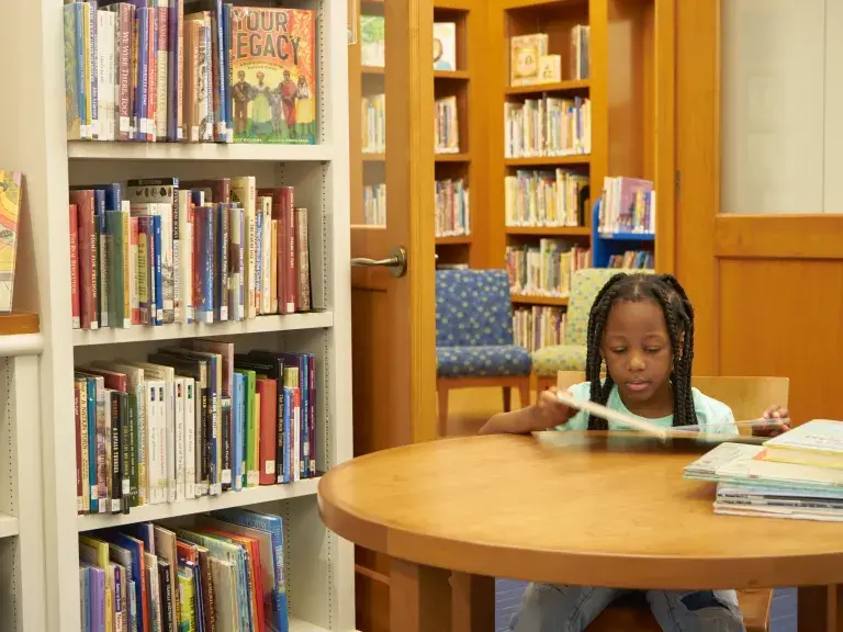 young girl reading a book at a circle table in the kid's library section