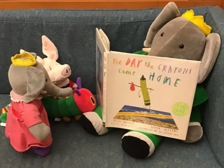 A soft toy Babar reads THE DAY THE CRAYONS CAME HOME to other soft toys
